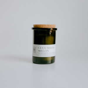 professionally styled photo of a candle in a glass green jar with a cork lid and a white label.