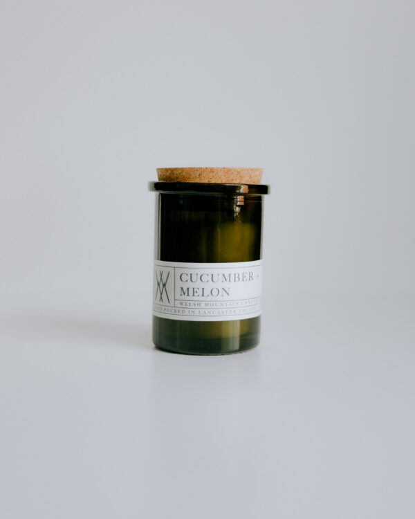 professionally styled photo of a candle in a glass green jar with a cork lid and a white label.