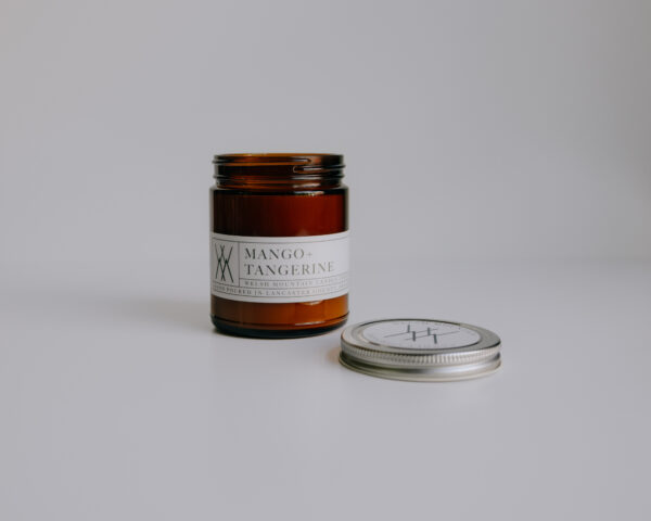 professionally photographed candle in amber colored glass jar with lid taken off.